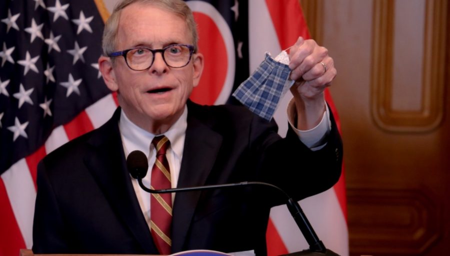 Mike DeWine holding up a cloth mask while giving a speech about Covid-19